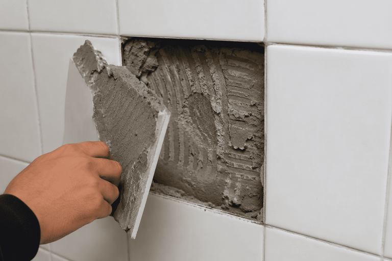 Azulejo desprendido de una pared que muestra una aplicación irregular del adhesivo durante la instalación.